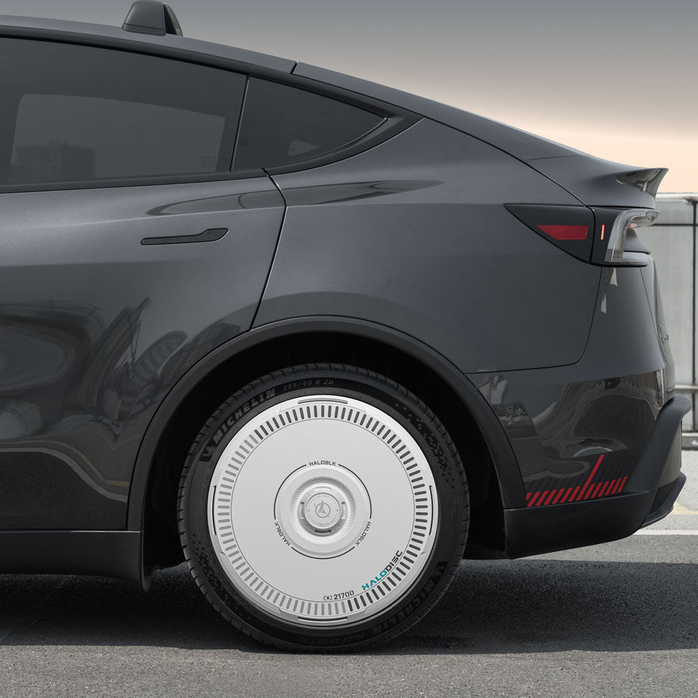 A close-up of the rear of a dark gray Tesla Model Y with HALODISC 2 Wheel Covers by HALOBLK Store, designed for Juniper 20" Helix 2.0 wheels. The unique silver disc-style cover features detailed markings and text around its edge.