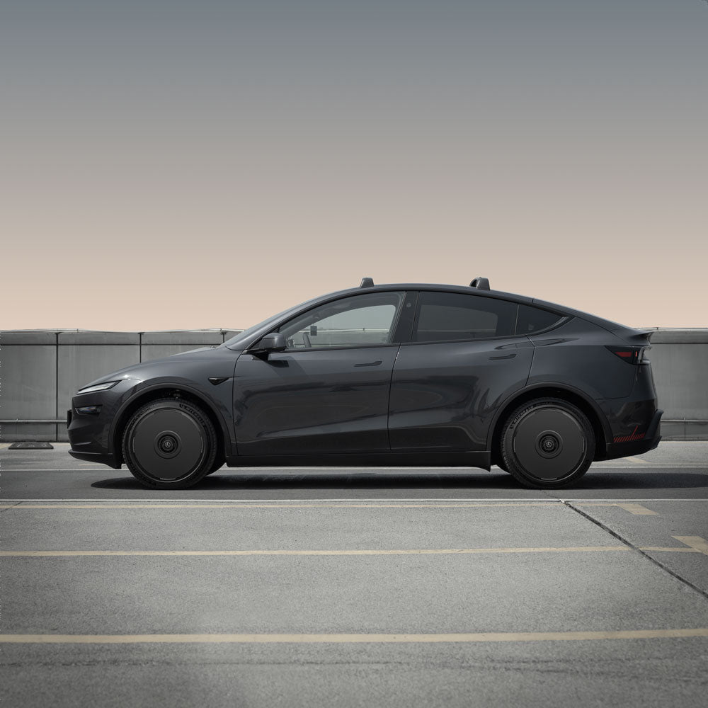 A sleek Tesla Model Y with HALODISC 2 Wheel Covers by HALOBLK Store is parked in an empty rooftop lot, viewed from the side against a muted sky and concrete barrier.