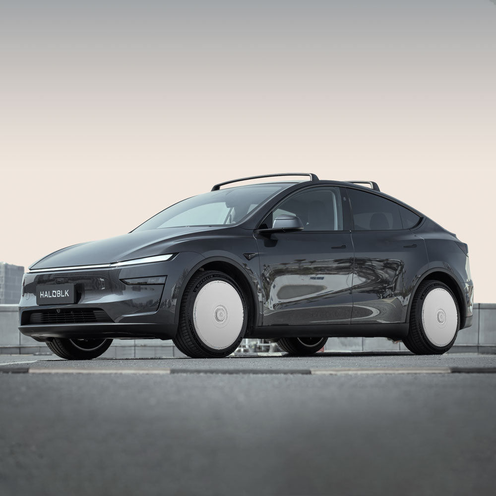 A sleek Tesla Model Y with HALODISC 2 Wheel Covers by HALOBLK Store on 20" Helix 2.0 wheels is parked on a rooftop, cityscape in the background beneath an overcast sky.