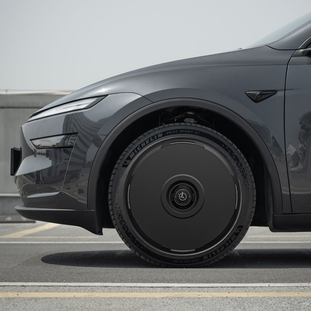 Close-up side view of a dark gray Tesla Model Y with HALODISC 2 Wheel Covers (Juniper 20" Helix 2.0 Wheels) by HALOBLK Store, focusing on the sleek solid black aerodynamic cover on the front left wheel, parked outdoors under clear skies.