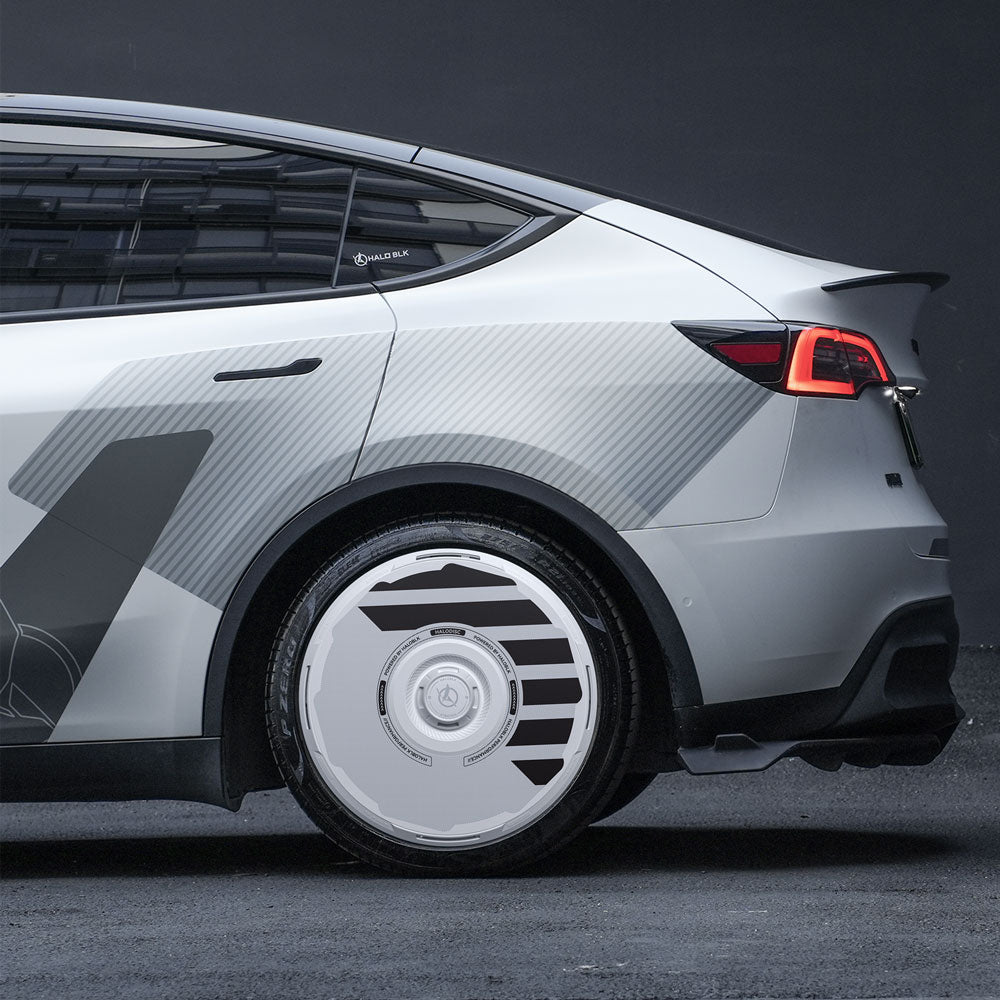 A close-up of a silver car’s rear showcases HALODISC 2 Wheel Covers by HALOBLK Store, designed for Tesla Model Y 21" Überturbine Wheels, featuring a futuristic geometric pattern with white sci-fi-inspired covers and dark accents.