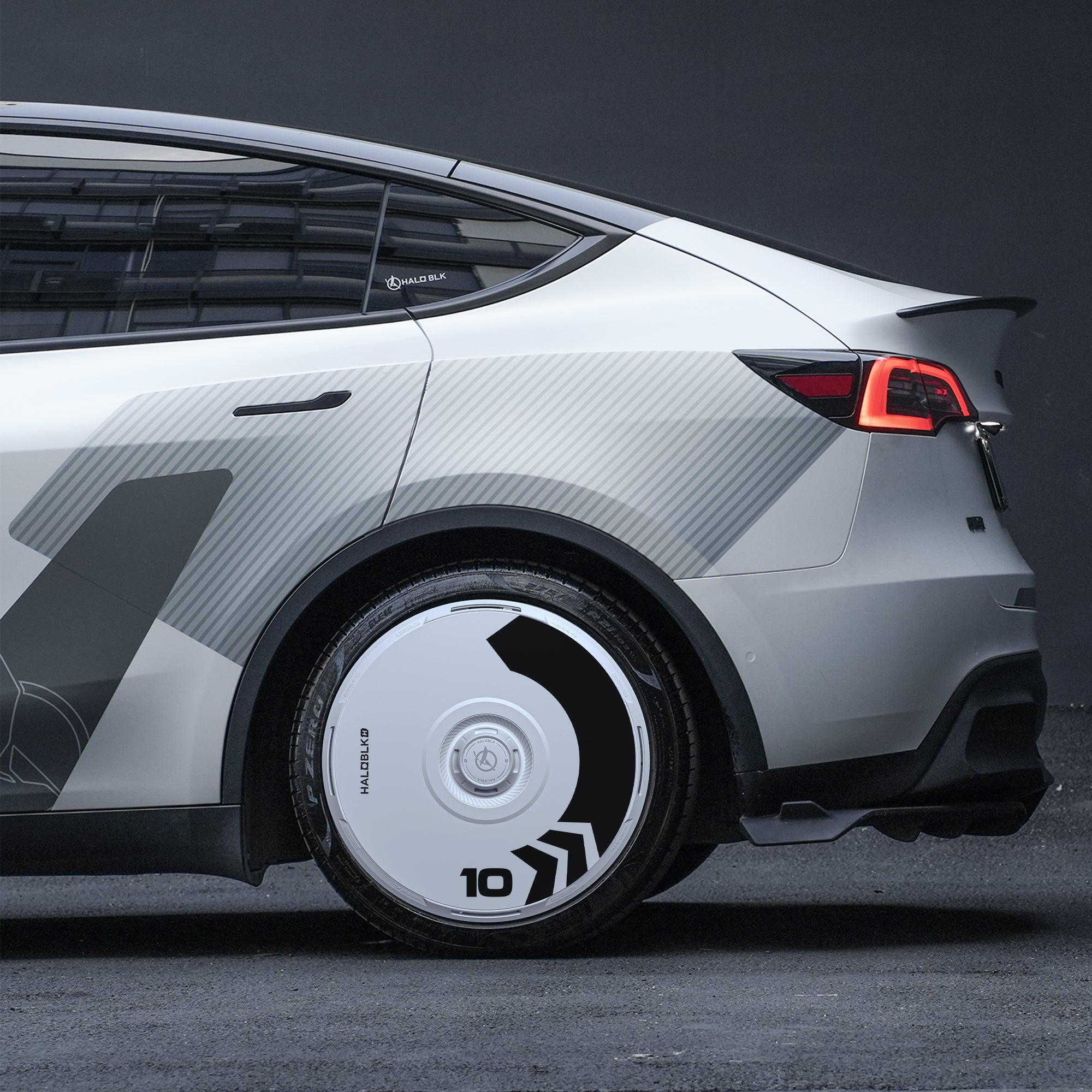 A close-up of the rear of a futuristic white car featuring HALODISC 2 Wheel Covers (Arrow) by HALOBLK Store for Tesla Model Y 21" Überturbine Wheels, showcasing a unique geometric wrap and minimalistic dark background.