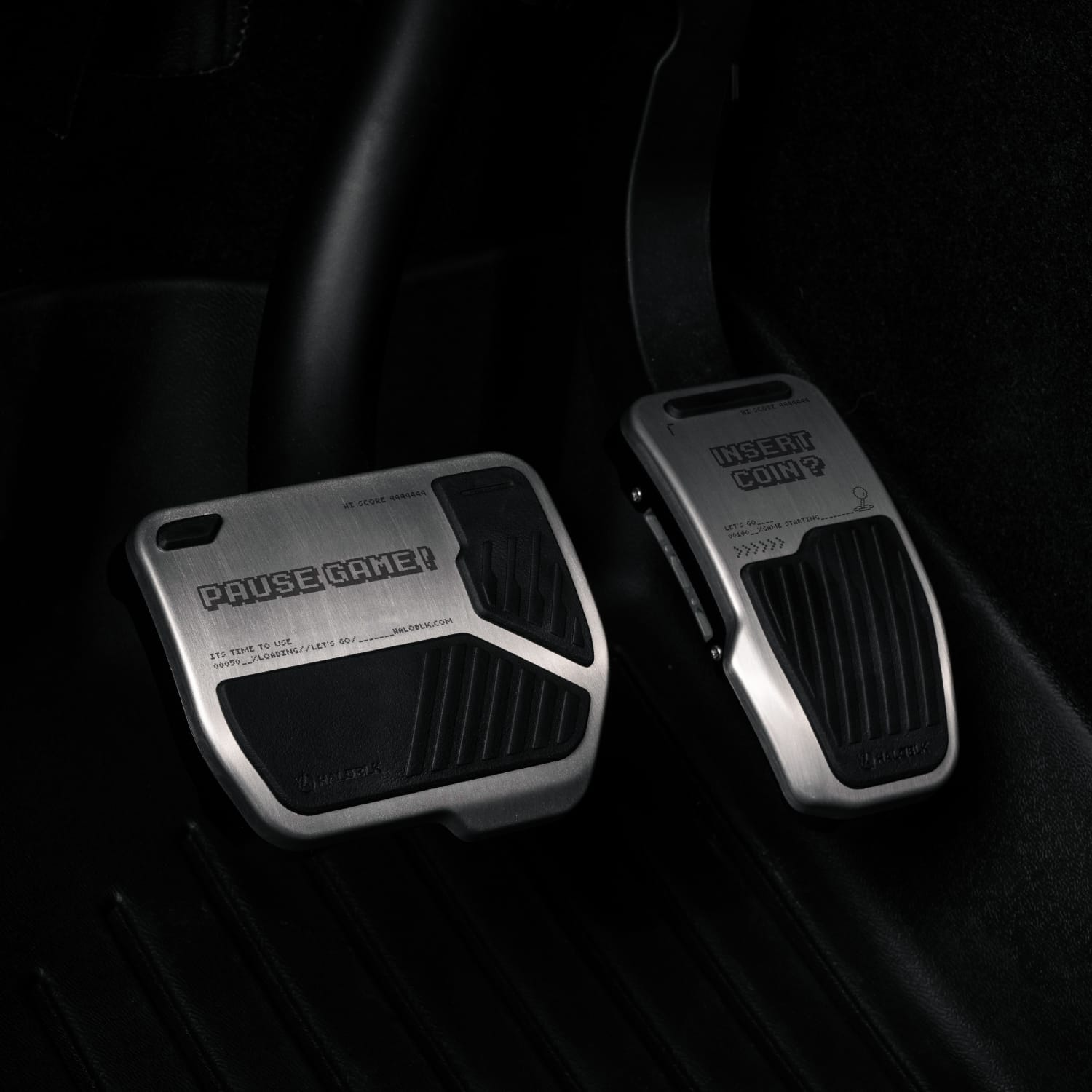 The HALOBLK Store's Alloy Pedals 2 for Tesla | ArcadeKid features metallic pedals with black rubber grips: the brake says "PAUSE GAME!" and the accelerator reads "INSERT COIN?", photographed against a dark car interior.