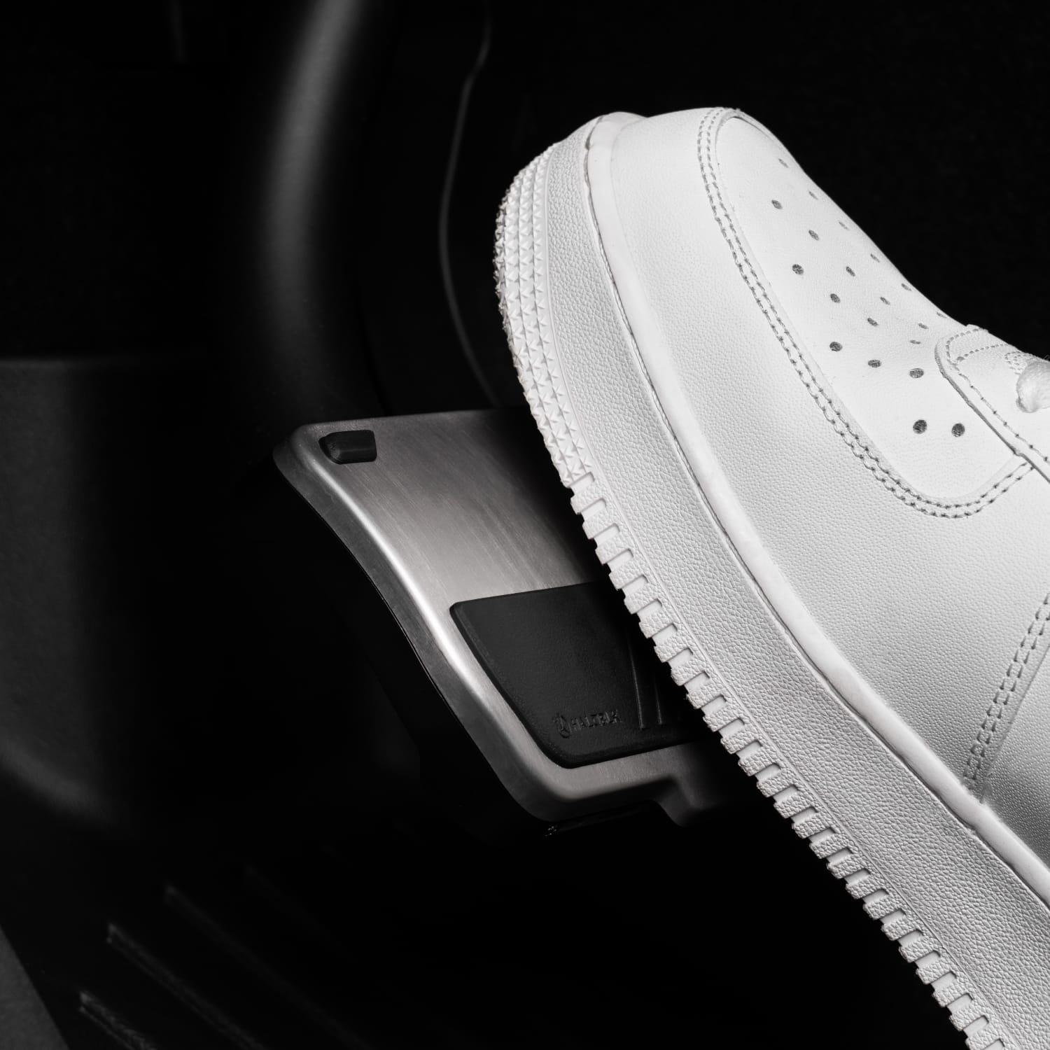 A close-up of a person wearing white sneakers pressing the accelerator pedal of Alloy Pedals 2 for Tesla by HALOBLK Store.