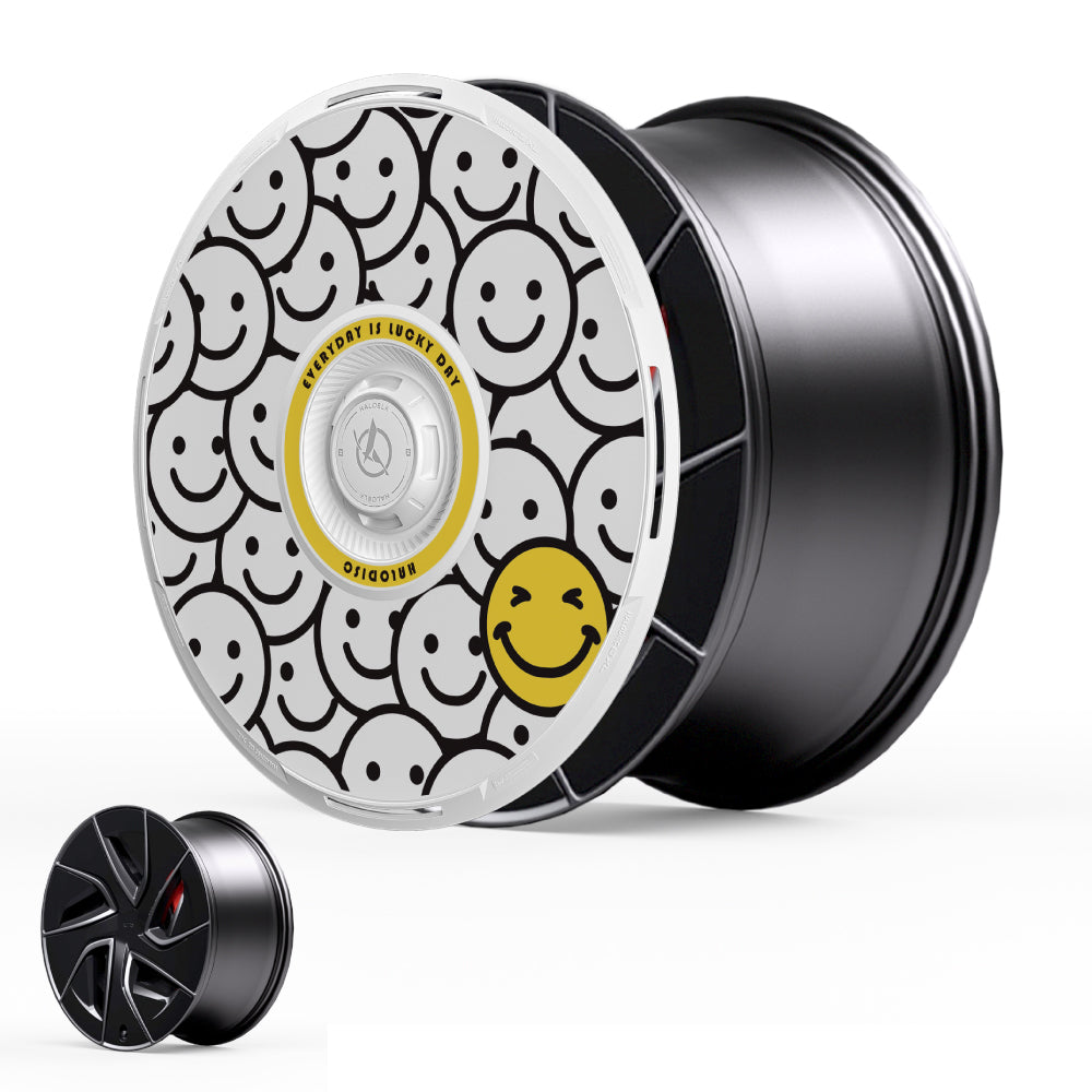 The HALODISC 2 Wheel Covers for Tesla Model S 19" Magnetite Wheels by HALOBLK Store feature a black rim with a white face decorated with black smiley faces and a single yellow smiley face. A smaller plain black cover is displayed in the corner.