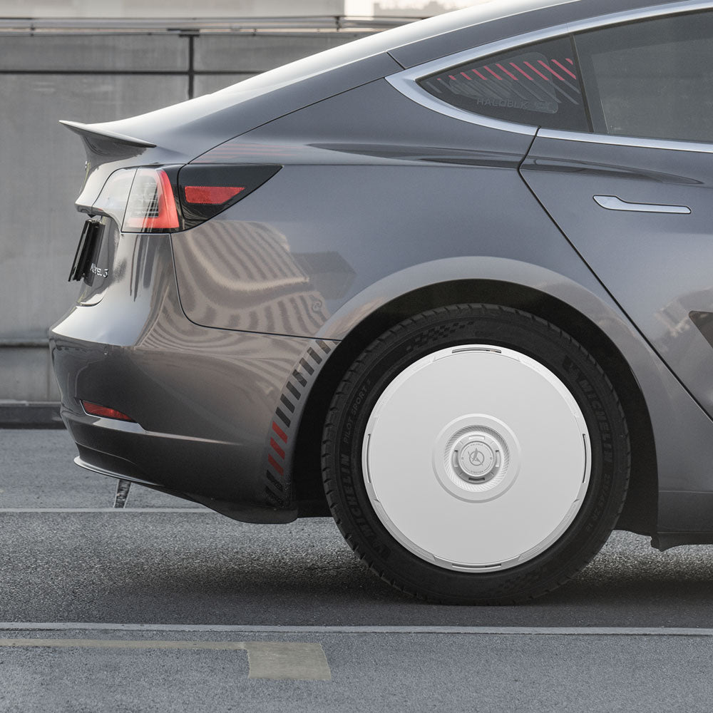 A close-up of a gray Tesla Model 3 (2021-2023) shows HALODISC 2 20" Überturbine wheel covers by HALOBLK Store on the rear tire, parked by a concrete wall and railing.