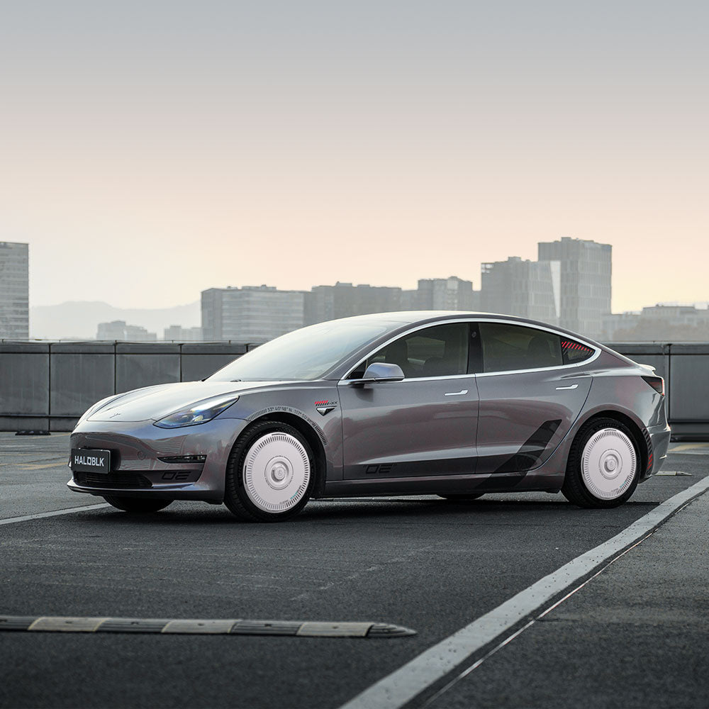 A grey Tesla Model 3 (2021-2023) with HALODISC 2 Wheel Covers by HALOBLK Store is parked on a rooftop at dusk, city skyline and tall buildings in the background.