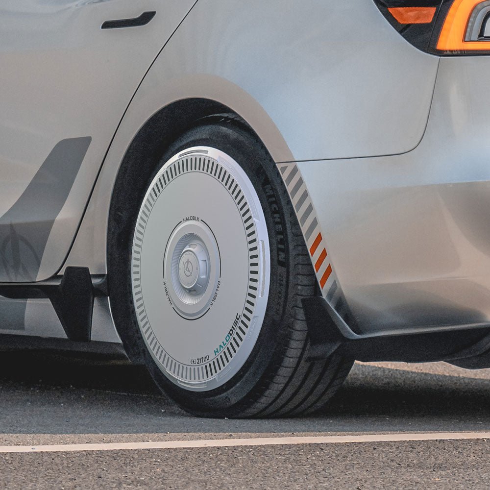 Close-up of HALODISC 2 Wheel Covers by HALOBLK Store on Tesla Model 3 Highland 18" Photon Wheels. Features sleek silver finish, futuristic hubcap design, and sharp lines with orange accents near the tail light and wheels.