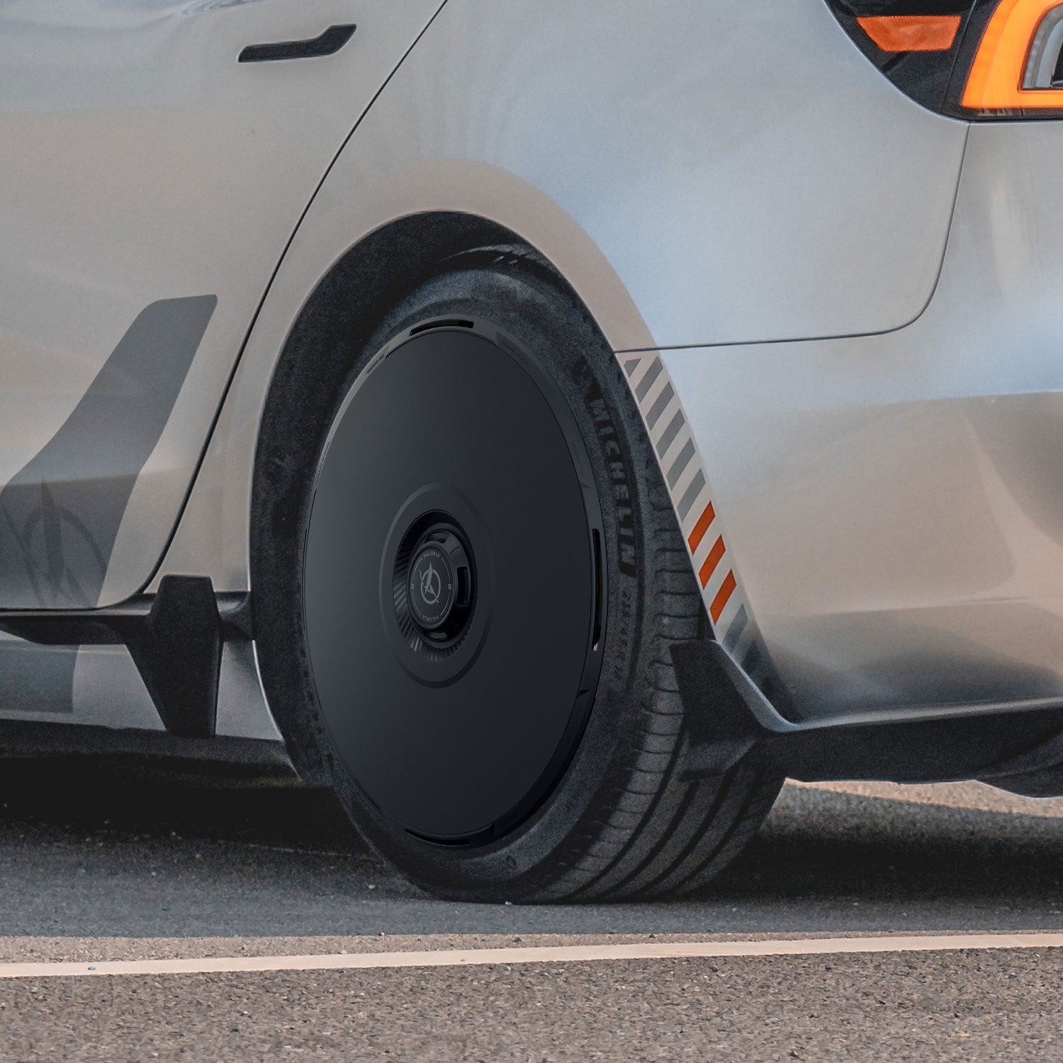 Close-up of the rear side of a silver Tesla Model 3 Highland with HALODISC 2 Wheel Covers by HALOBLK Store on 20" Warp Wheels. The black aerodynamic cover and orange-gray striped accents near the rear wheel arch are visible.