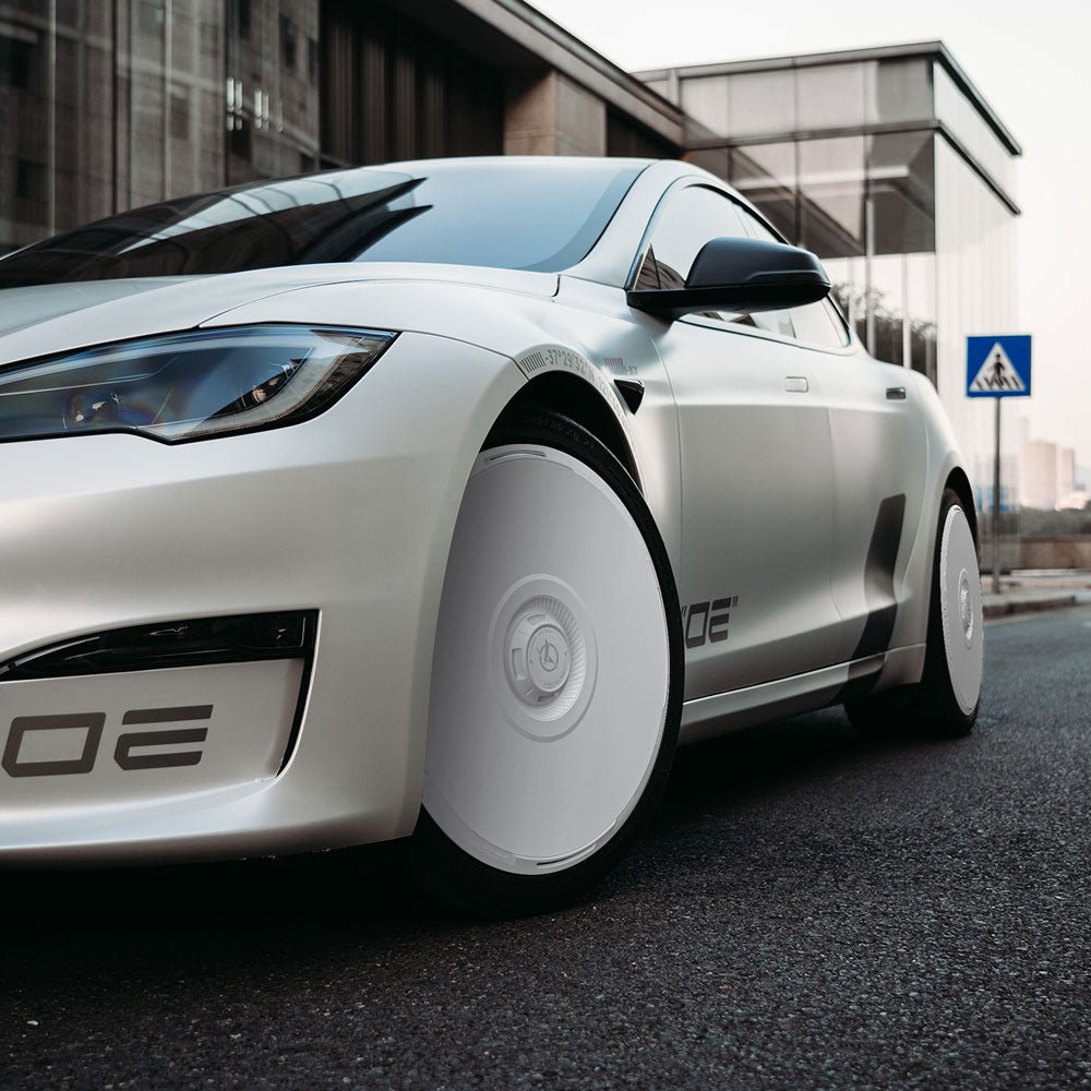 A Tesla Model S with HALODISC 2 Wheel Covers (21" Arachnid) from HALOBLK Store is parked on a street near a modern glass building and a pedestrian crossing sign.