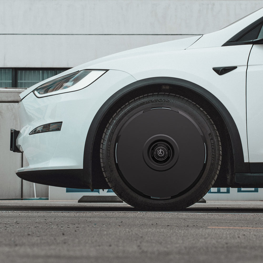Close-up side view of a white Tesla Model X (2016-2020) with a solid black HALODISC 2 aerodynamic wheel cover (HALOBLK Store) on the 20" Slipstream wheel; part of a building and pavement appear in the background.