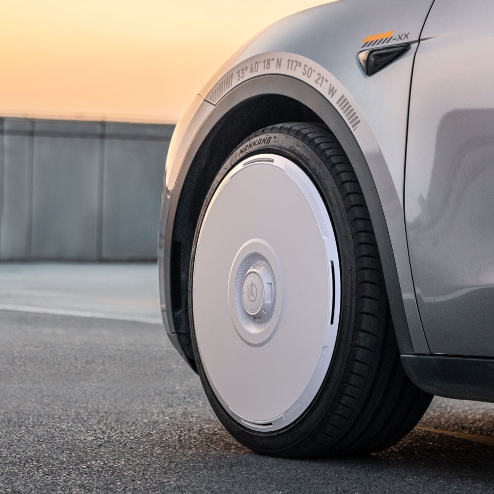 A close-up of a Tesla Model Y's front wheel showcases HALODISC 2 Wheel Covers by HALOBLK Store, featuring a white, futuristic circular hubcap design. Geographical coordinates are marked on the fender above the wheel.