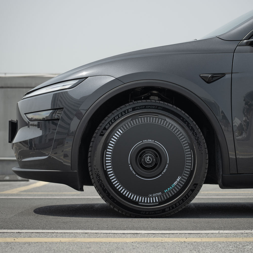 Side view of a Tesla Model Y with HALODISC 2 Wheel Covers by HALOBLK Store, featuring a black, futuristic design with digital-like markings and green accents, installed on 20" Helix 2.0 Juniper wheels, parked roadside under clear skies.